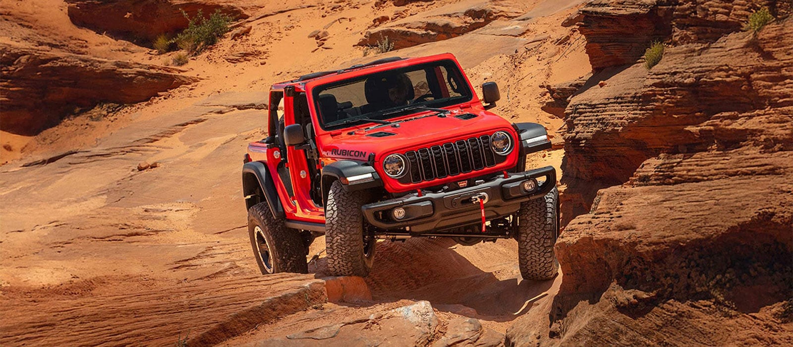 A red Jeep Wrangler driving over a rocky area.