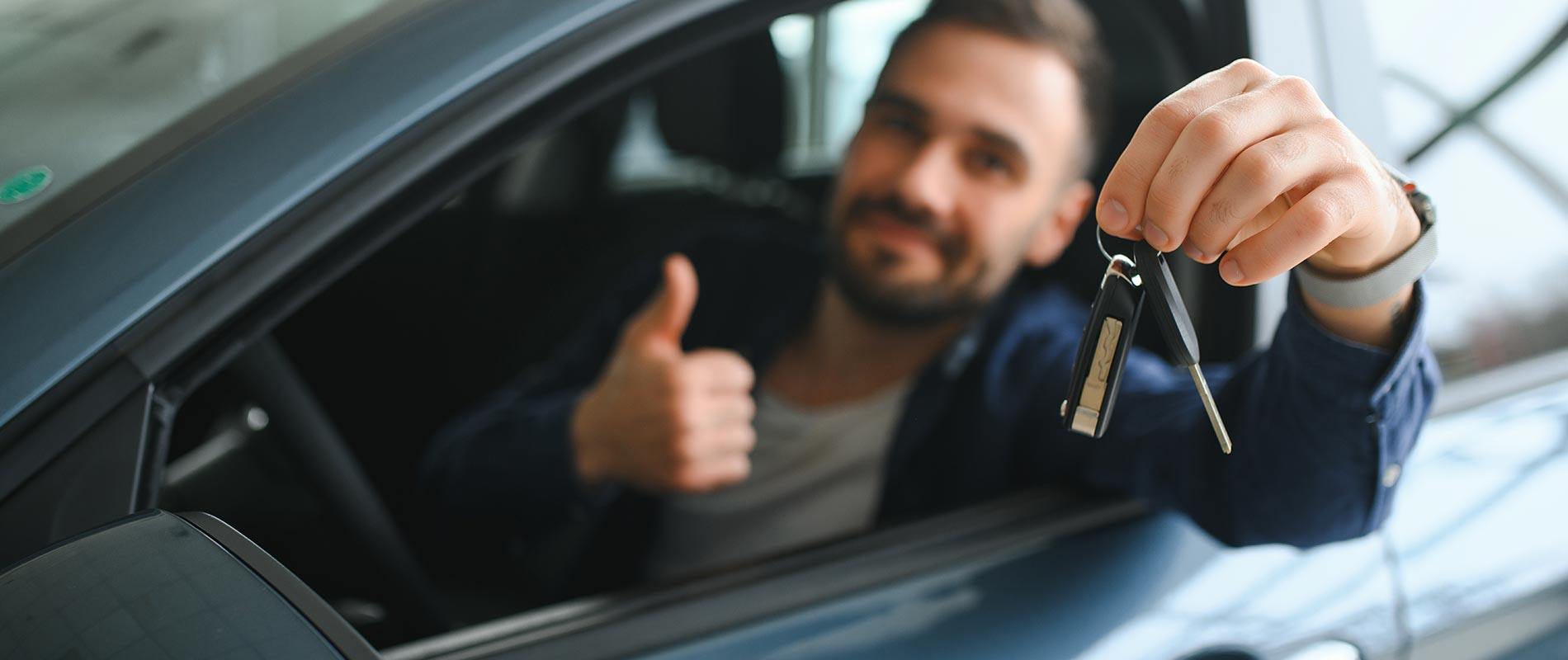 Young man showing off his car keys and giving a thumbs up from the driver's seat.