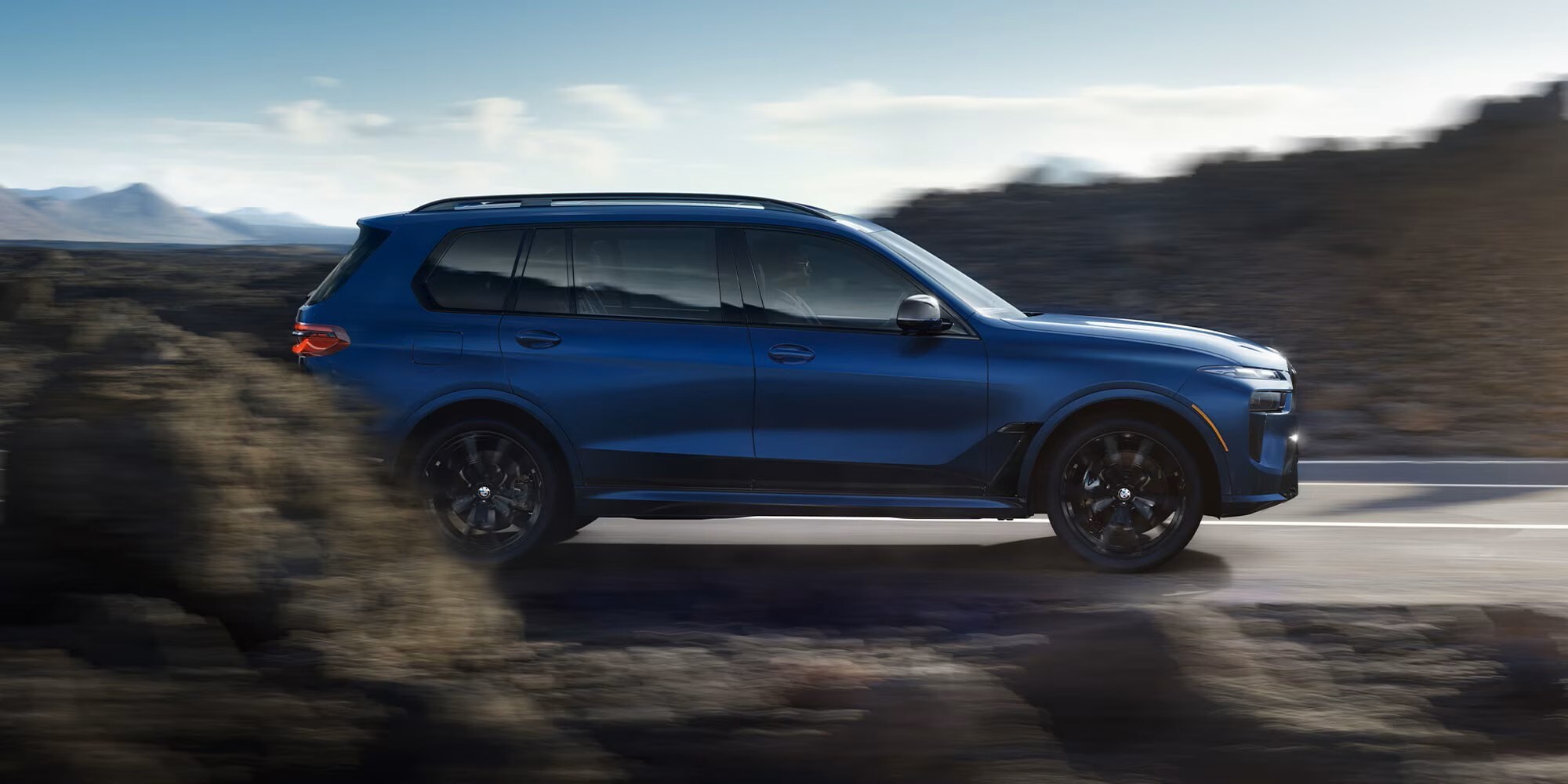 a blue 2025 bmw X7 M60i SUV driving in the desert with its background blurred