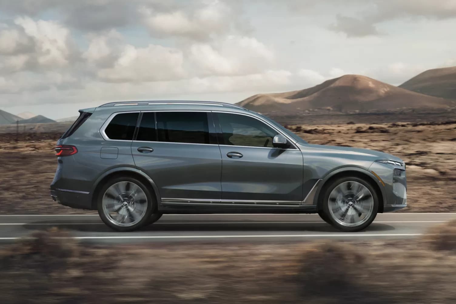 A silver bmw x7 driving on the road.