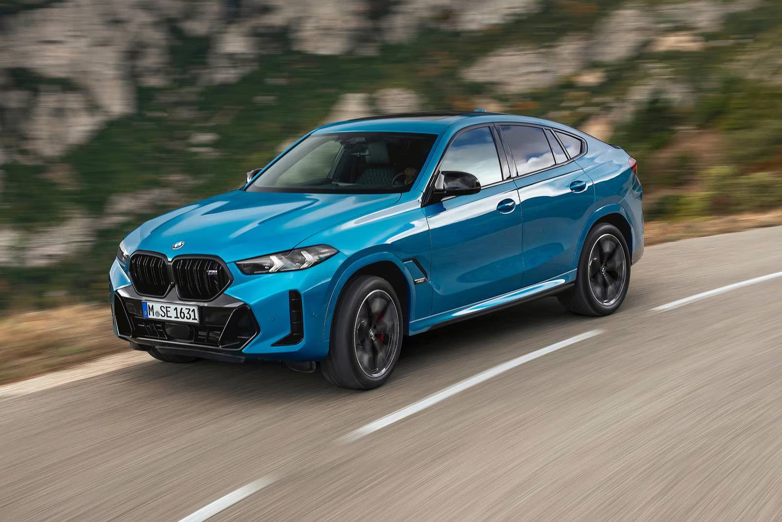 A blue bmw x6 m60i driving on the road.