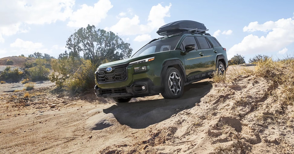 Green Subaru SUV with roof box driving on a sandy trail.png