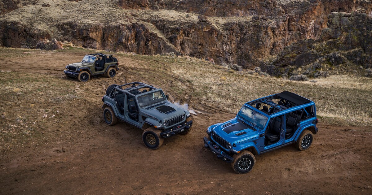 Three Jeep Wranglers in different colors parked around each other on a dirt road.