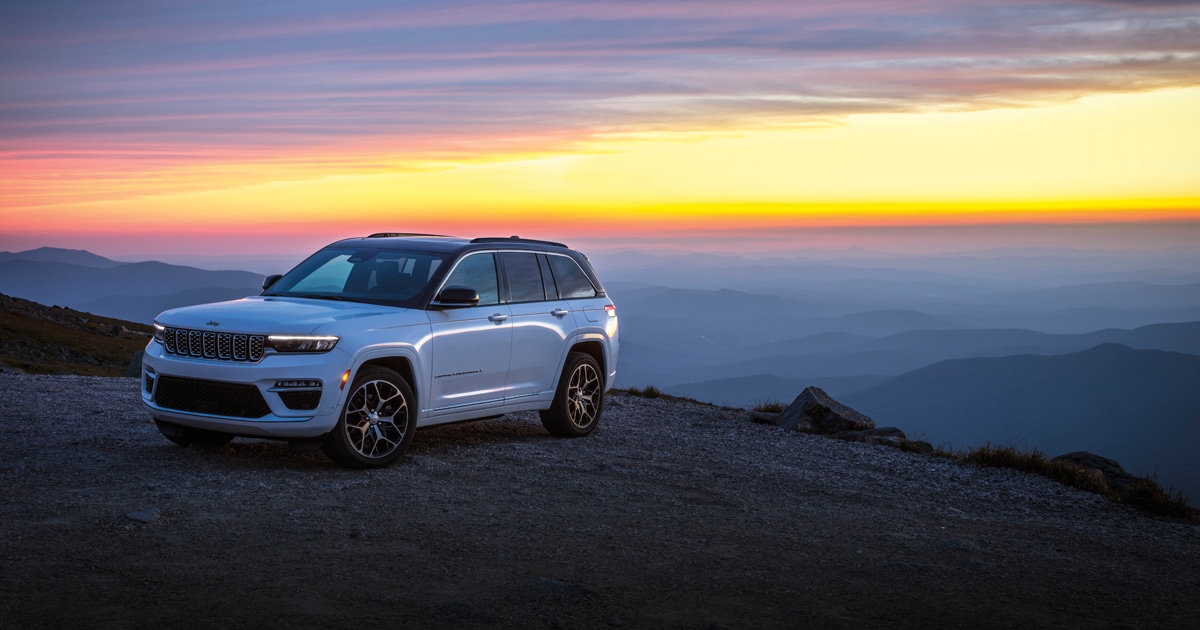 A Jeep Grand Cherokee parked on top of a mountain at sunset