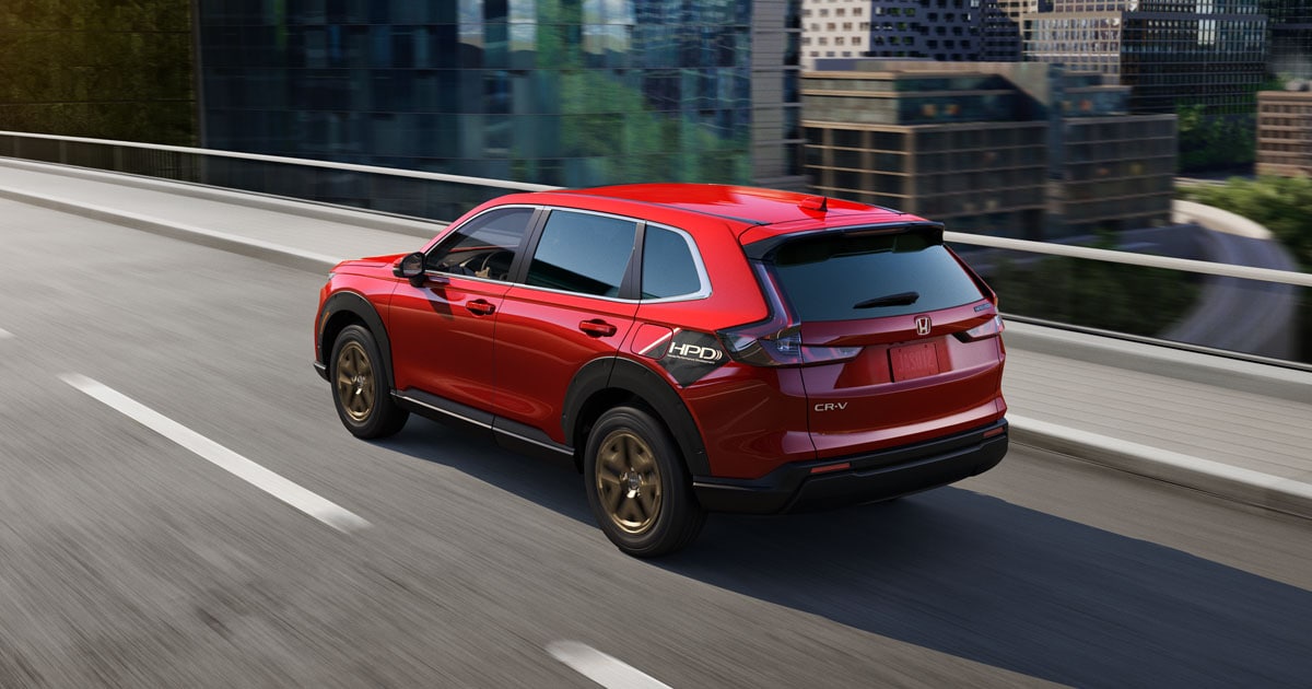 A red Honda CR-V Hyrbrid driving on the highway through a city.