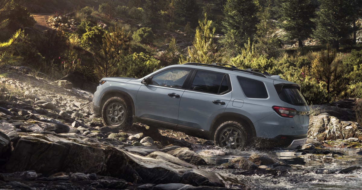 A silver 2025 Honda Pilot driving off-road up a rocky hill.