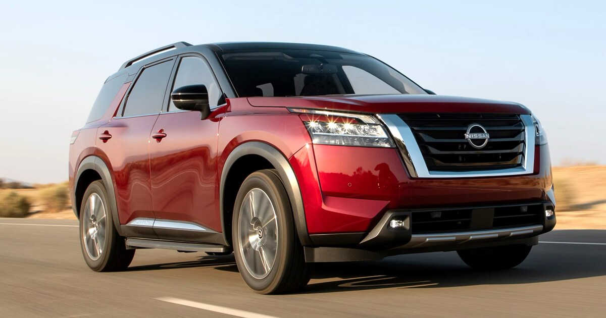 A 2024 Nissan Pathfinder in the 2-tone scarlet ember tintcoat and super black driving down a road in the desert.