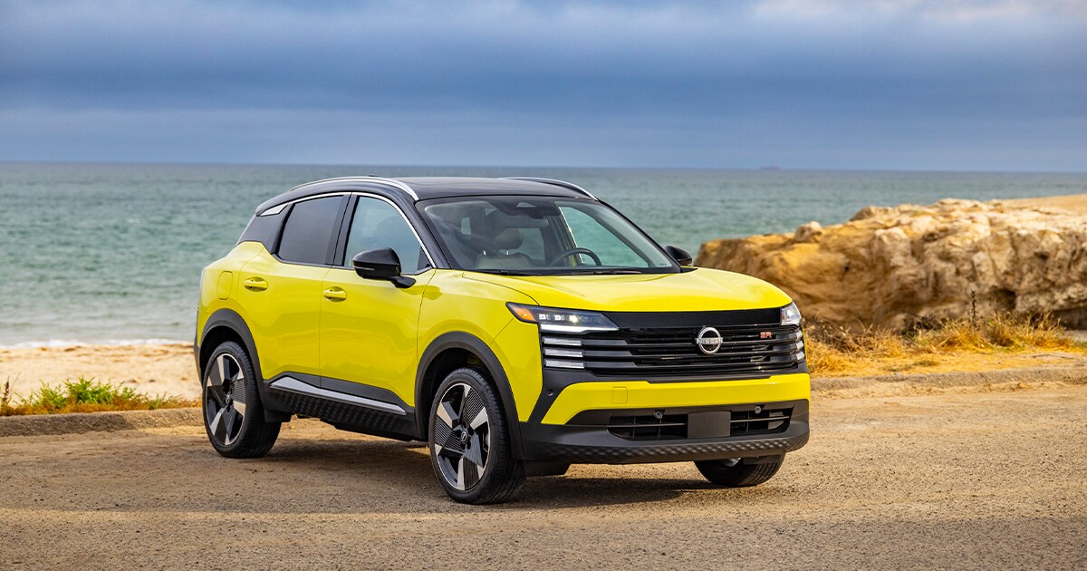 A yellow Nissan Kicks model with a black roof sits in front of a cloudy seashore.