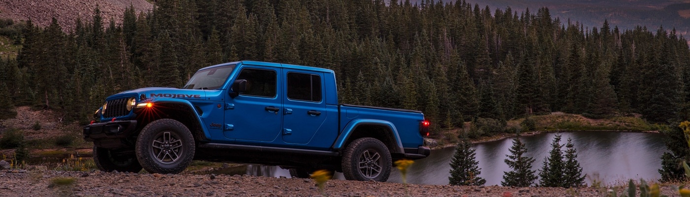 Blue Jeep Gladiator Mojave parked above a lake in the forest