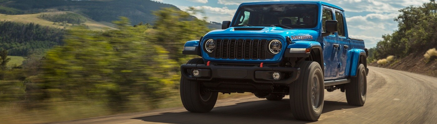 Blue Jeep Gladiator Mojave driving on a road in the forest
