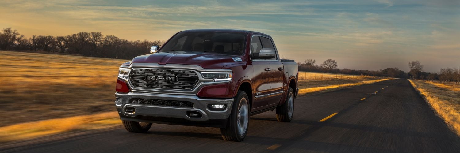 dark red Ram 1500 pickup truck driving past a field at dusk