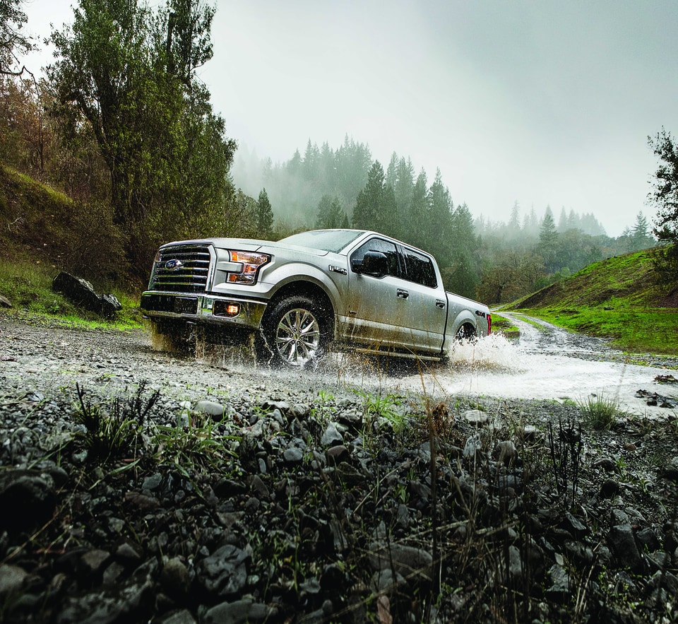 silver Ford F-150 truck getting up a steep, wet, rocky hill