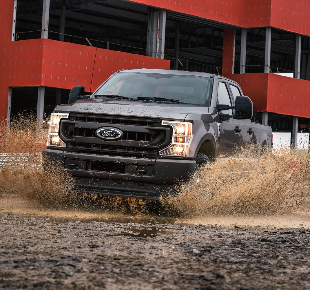 dark gray Ford F-250 commercial work truck splashing through the mud at a construction site