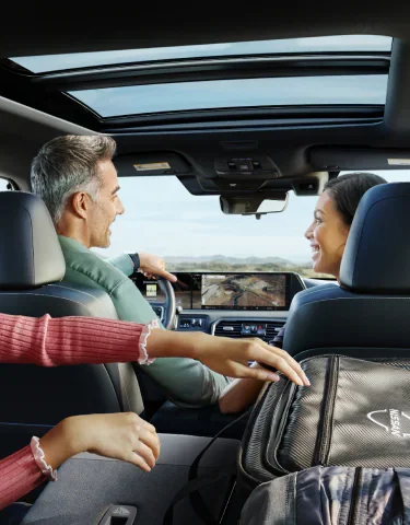 Open panoramic moonroof over the front seats of a 2027 Nissan Armada, with two people up front and a map on the center display