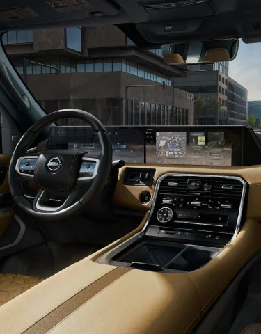 Front cabin of a 2027 Nissan Armada in tan leather showing the steering wheel, the driver display and the wide center touchscreen above the climate dials
