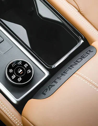 Close-up of the rotary drive and terrain mode dial on a Nissan Pathfinder center console, beside a trim panel embossed PATHFINDER