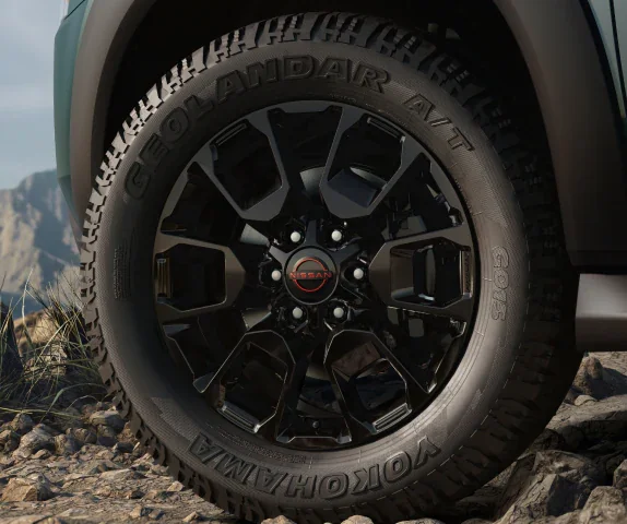 Close view of a black alloy wheel and Yokohama Geolandar all terrain tire on a 2027 Nissan Armada PRO-4X standing on broken rock