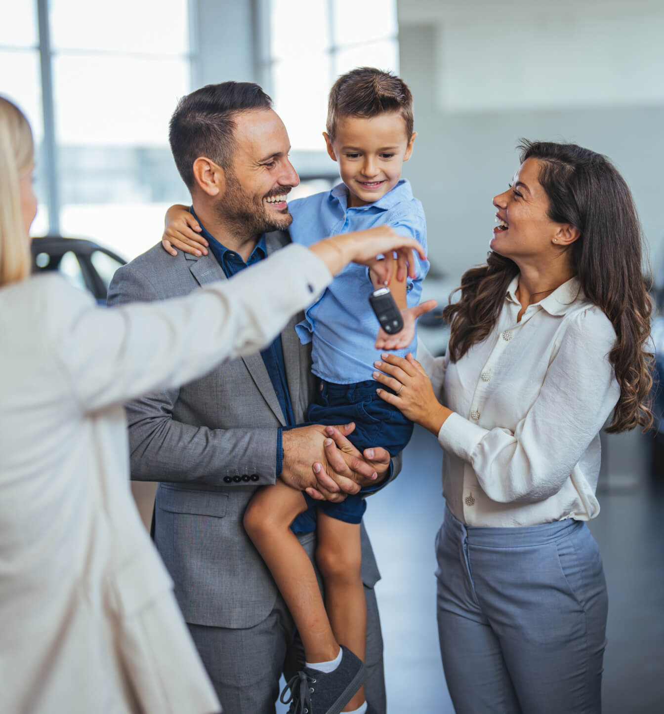 A woman hands a smiling family keys to a new car in a bright modern dealership.