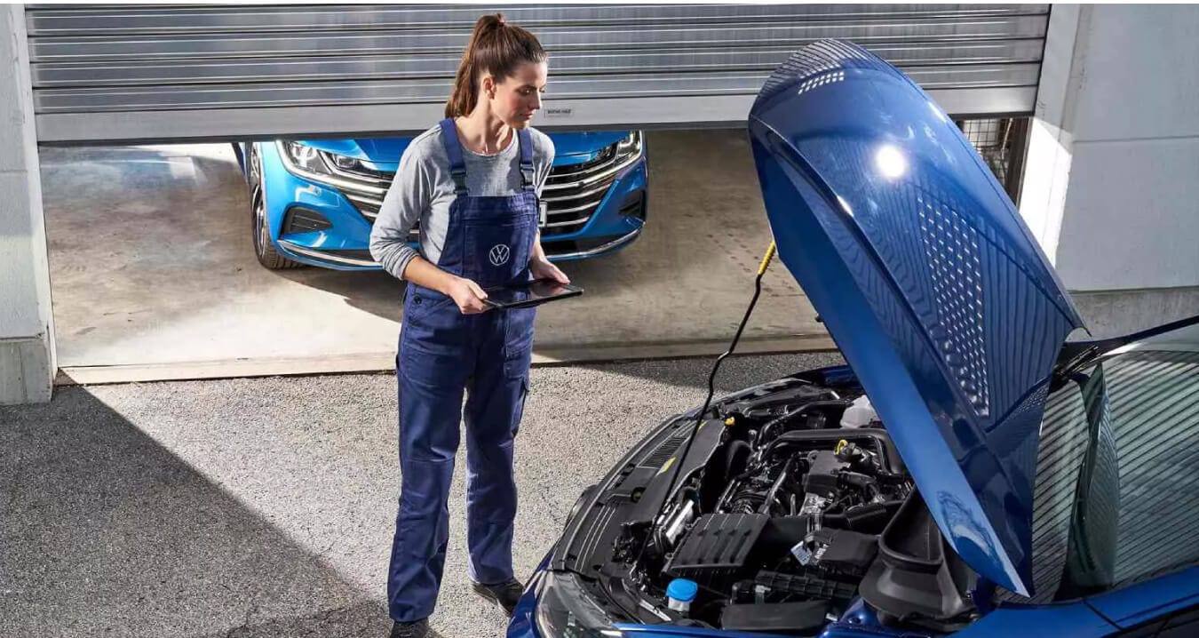 Volkswagen Golf R exterior in Lapiz Blue Metallic with service technician holding tablet under open hood at dealership.