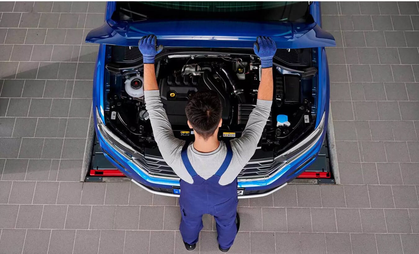 Volkswagen Taos SE exterior in Cornflower Blue with mechanic opening the hood inside a service bay.