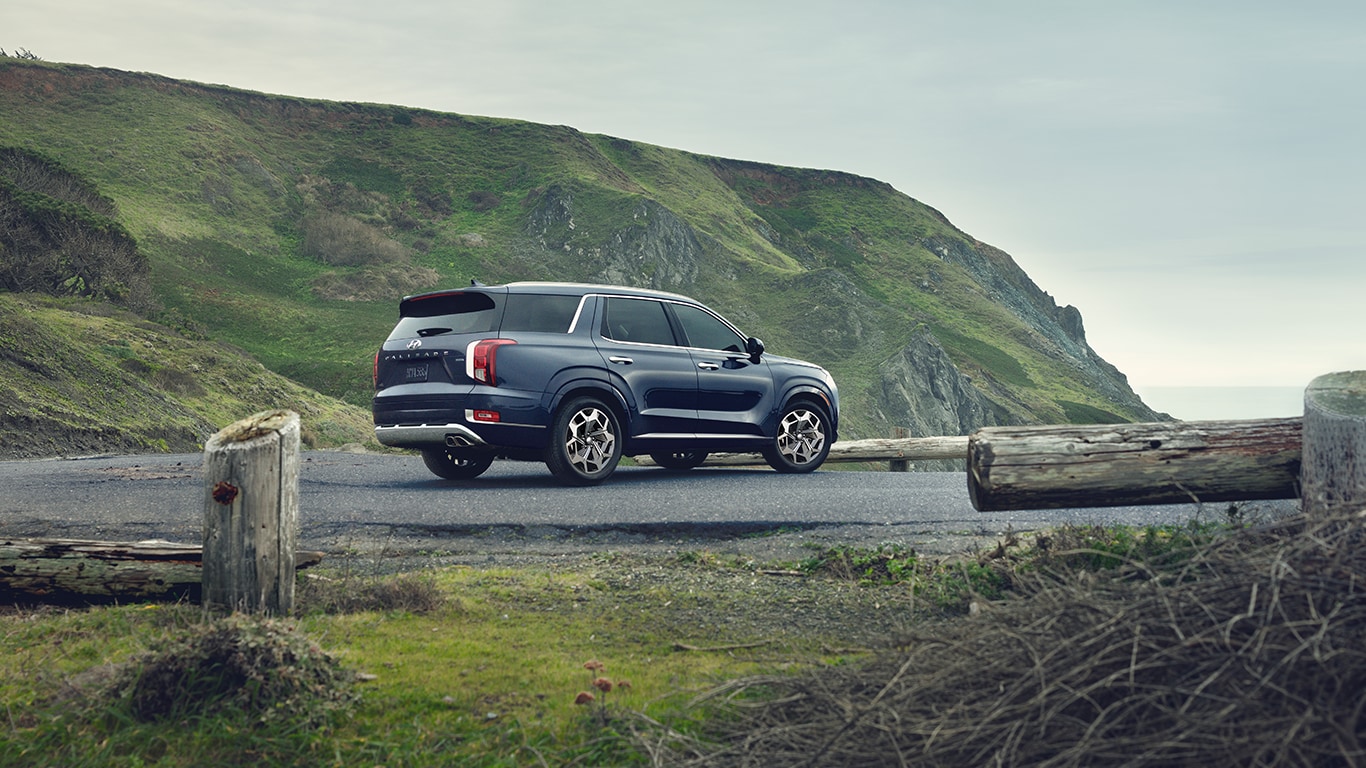 Haddad Hyundai is a Hyundai Dealership  near Pittsfield, MA | Rear view of a Navy blue Hyundai Palisade parked on a cloudy day with a mountain in the background 