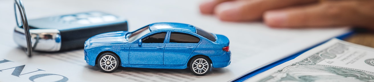 Defining GAP Insurance at Haddad Hyundai in Pittsfield, MA | Close up of a small blue toy car next to a pair of car keys while on top of some paperwork and cash