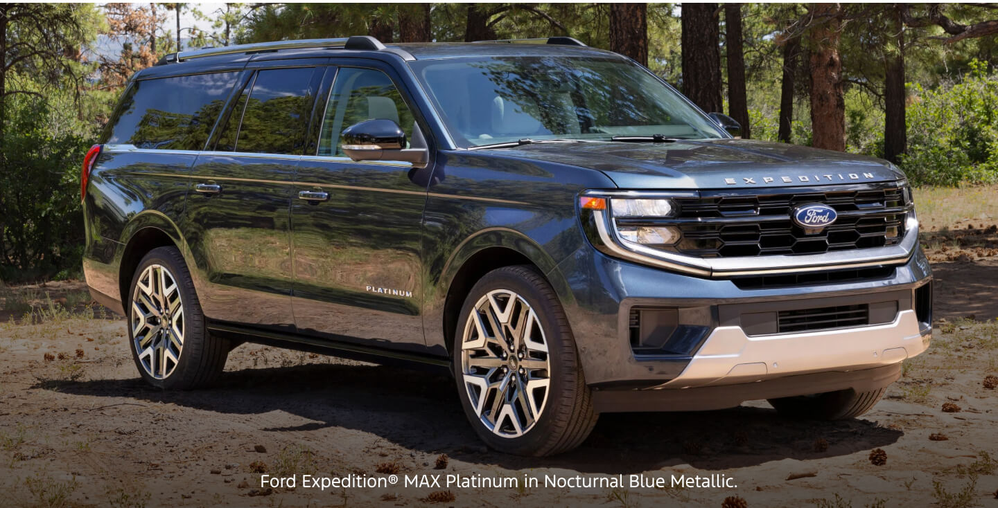 Side-profile view of a blue Ford Expedition MAX Platinum parked in a dirt clearing near a forest.