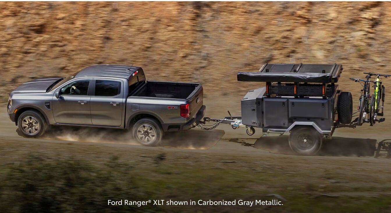 High-angle profile view of a 26 Ford Ranger XLT towing a camper trailer down a dusty dirt road.