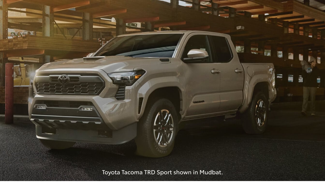 Front three-quarter view of a 26 Toyota Tacoma TRD Sport parked in an open-air lumberyard warehouse.