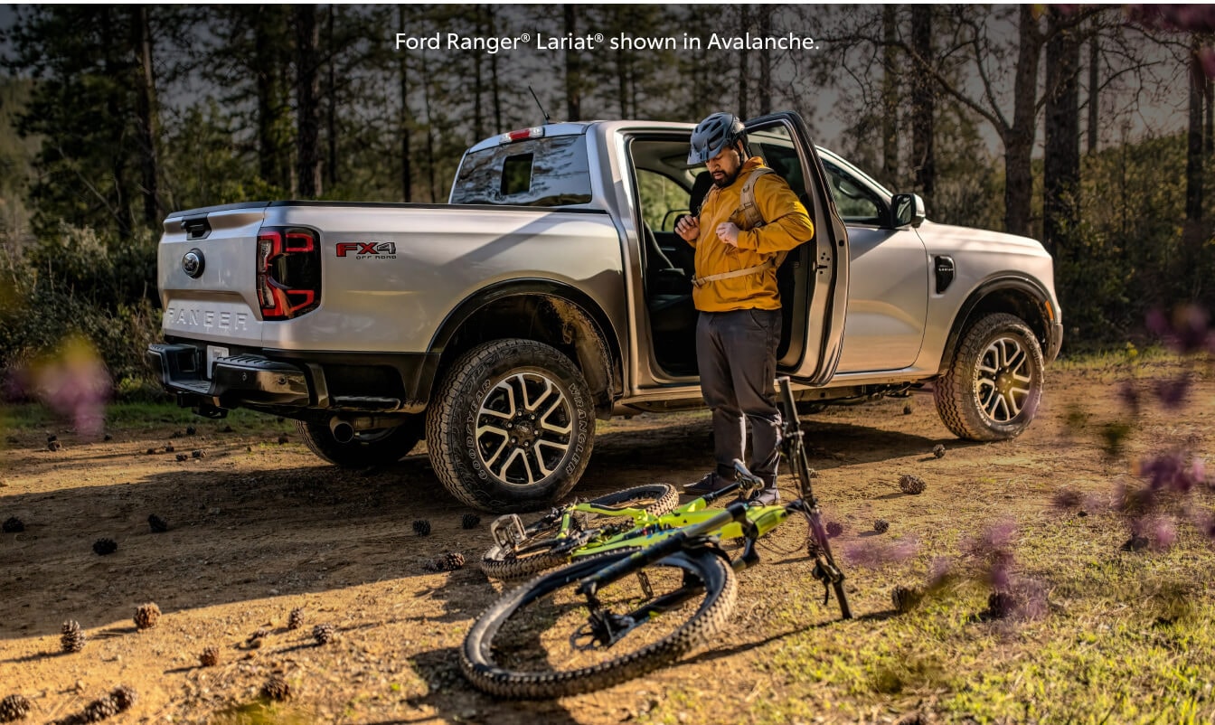 Rear three-quarter view of a 26 Ford Ranger Lariat parked as a cyclist stands beside.