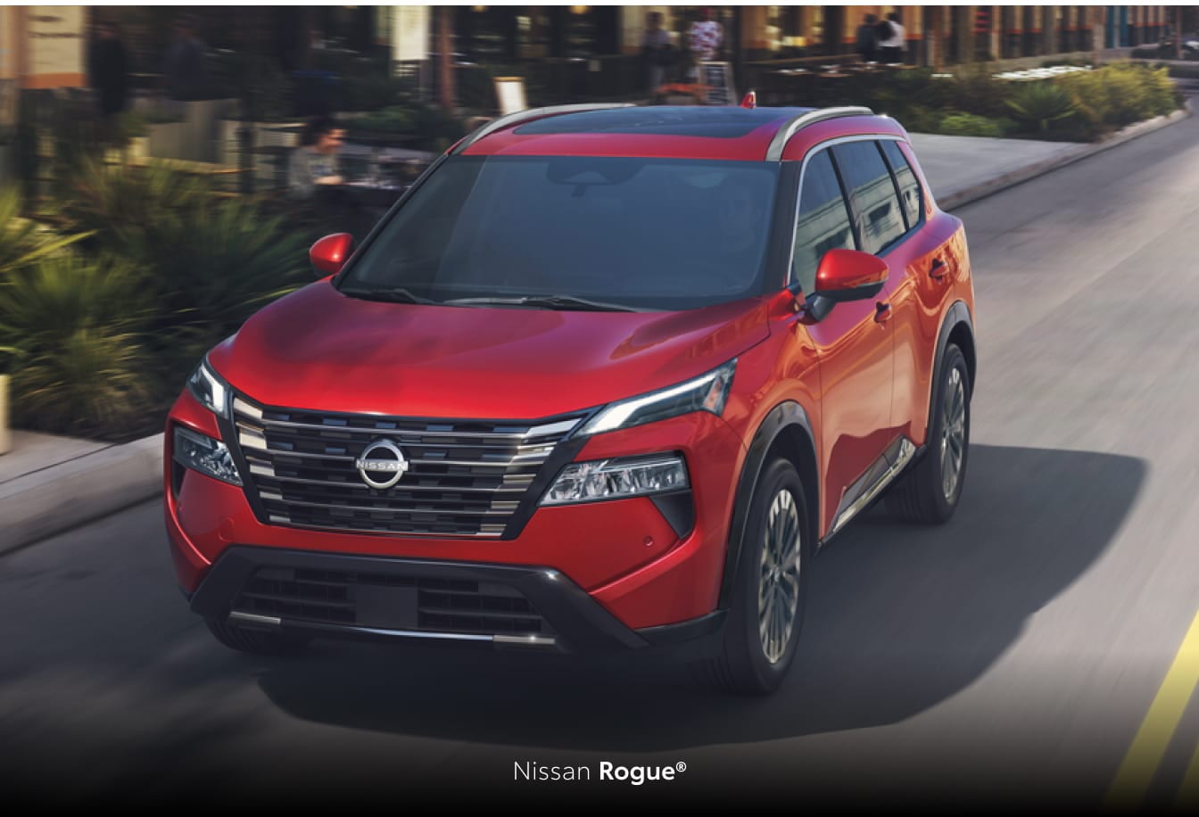 Red Nissan Rogue driving on a city street, shown from a front three-quarter angle.