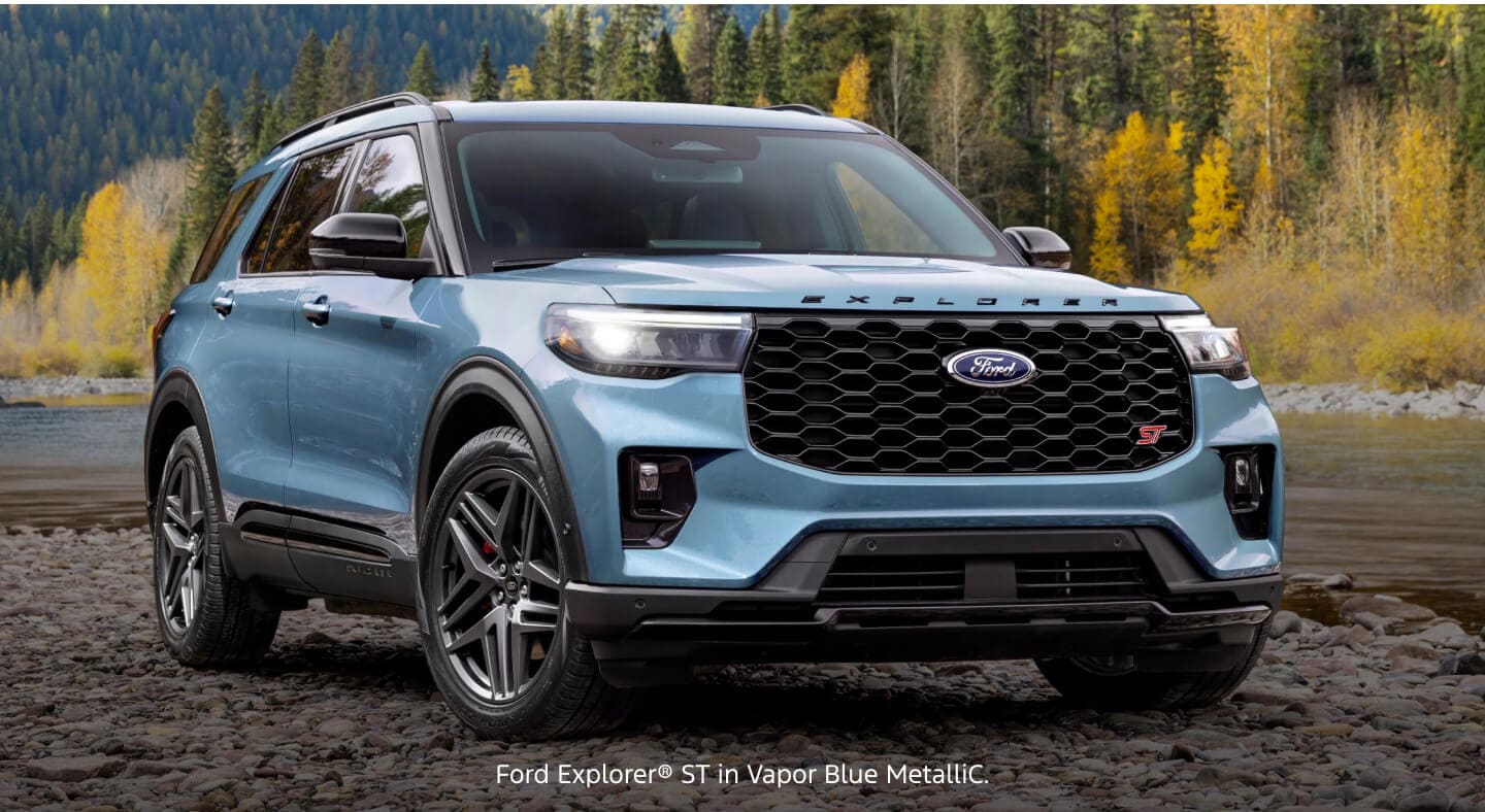 Three-quarter front view of a blue Ford Explorer ST parked on a rocky shoreline next to a river.