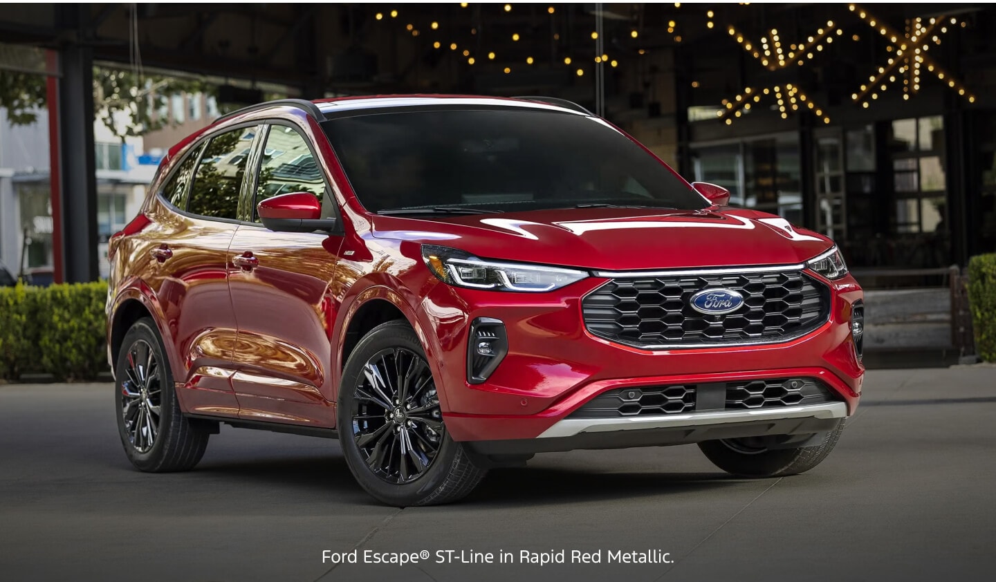 Three-quarter front view of a red Ford Escape ST-Line parked in front of a modern urban restaurant building.