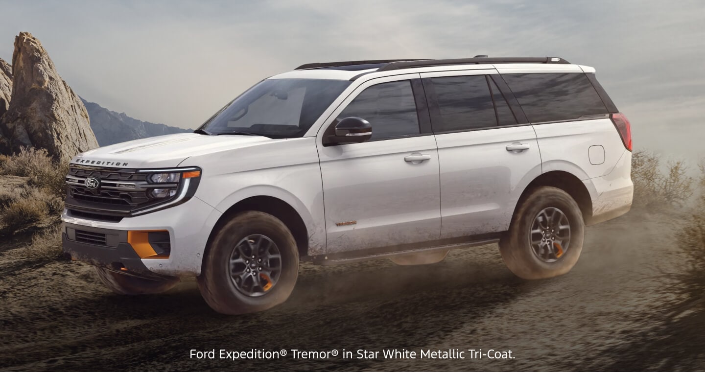 Three-quarter front view of a white Ford Expedition Tremor kicking up dust on an off-road hillside.
