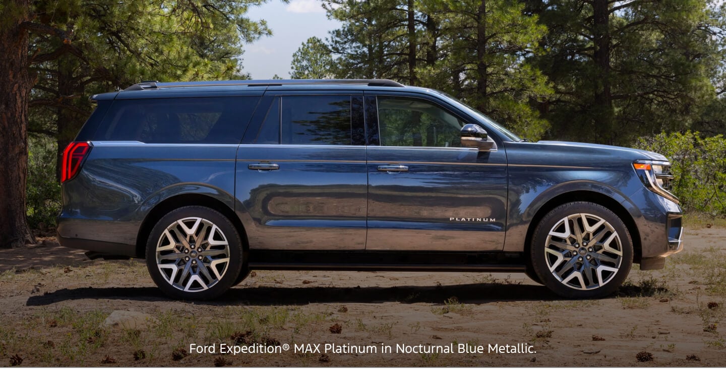 Side-profile view of a blue Ford Expedition MAX Platinum parked in a clearing surrounded by pines.