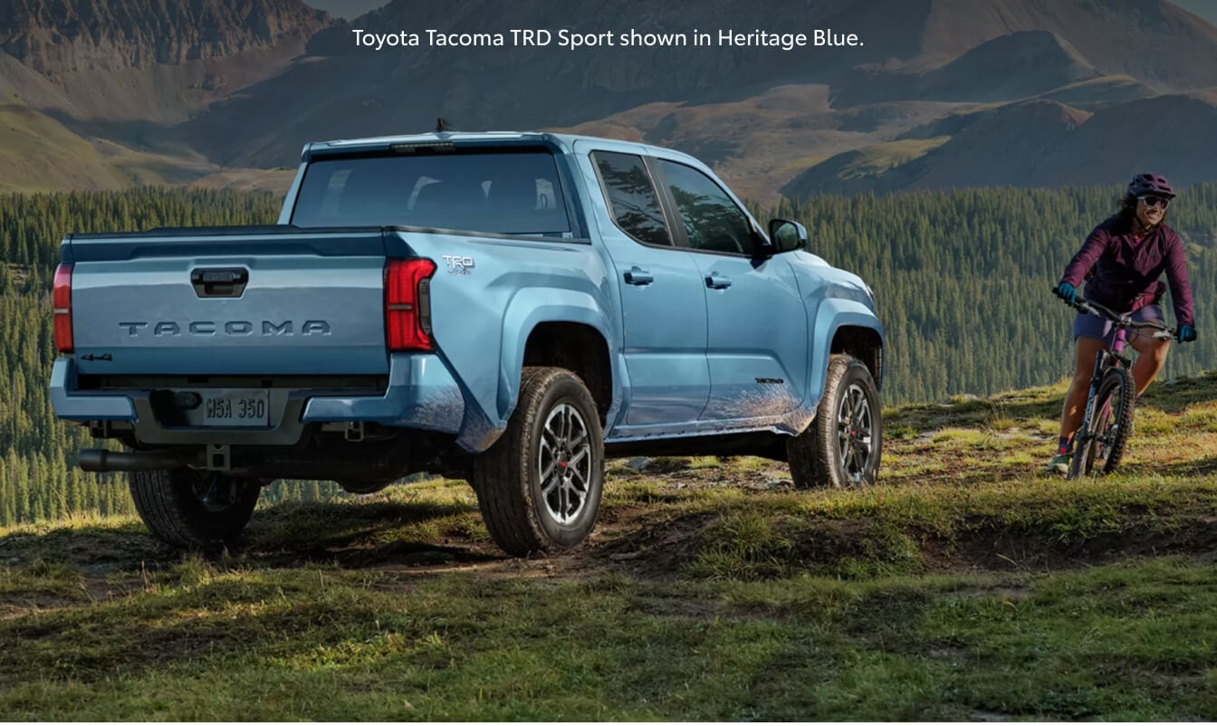 Rear three-quarter view of a 26 Toyota Tacoma TRD Sport on a grassy mountain trail.