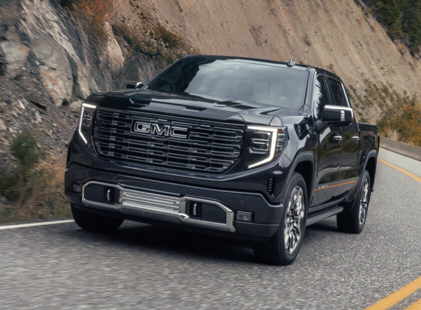 Low angle action shot of a black 2026 GMC Sierra driving down a mountain highway.