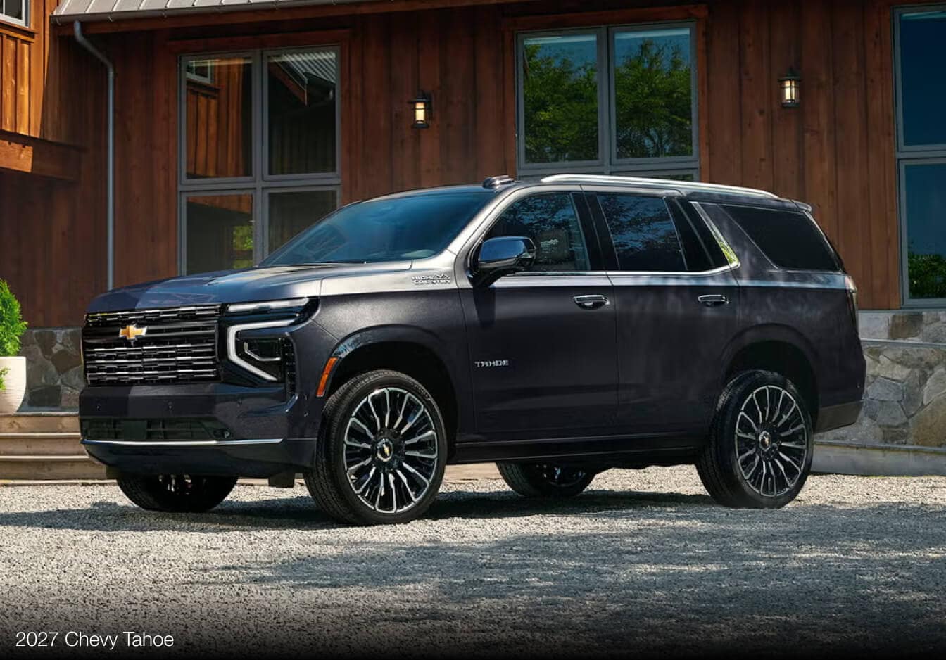External low angle image of a dark gray 2027 Chevy Tahoe parked in an upscale rustic driveway.
