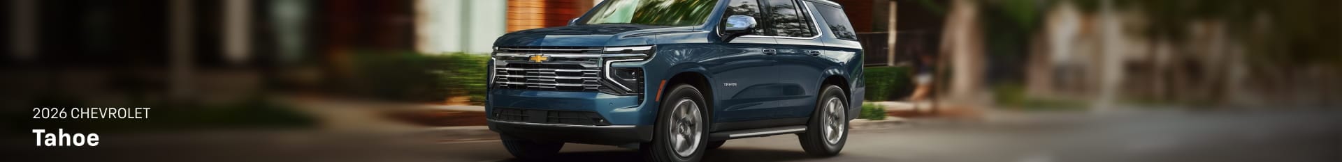 Blue 2026 Chevrolet Tahoe shown from a front three-quarter angle driving on a residential street.