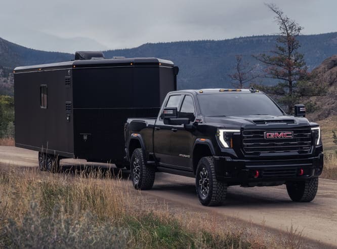 Black GMC Sierra 2500 HD towing a large trailer on a mountain road.