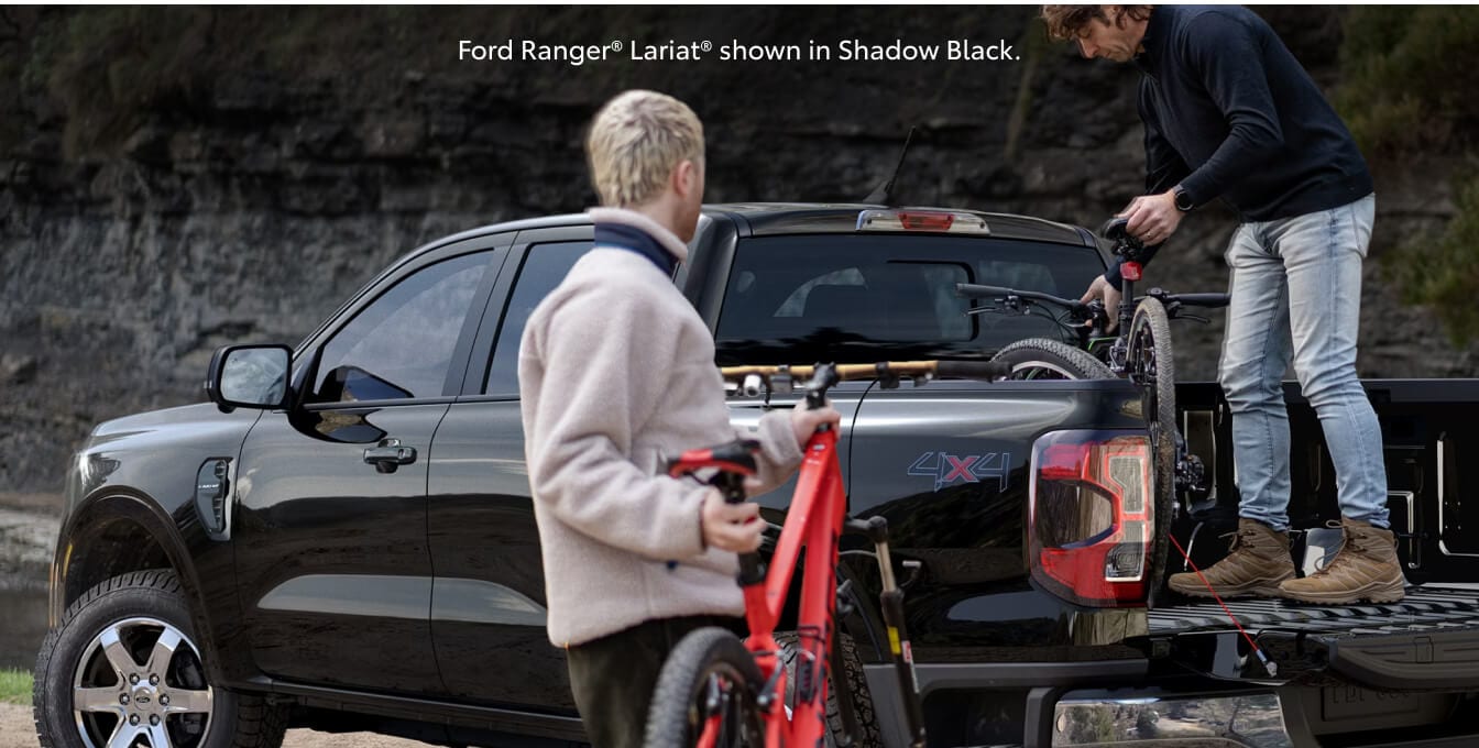 Three-quarter rear view of a 26 Ford Ranger Lariat with open tailgate as cyclists load mountain bikes.