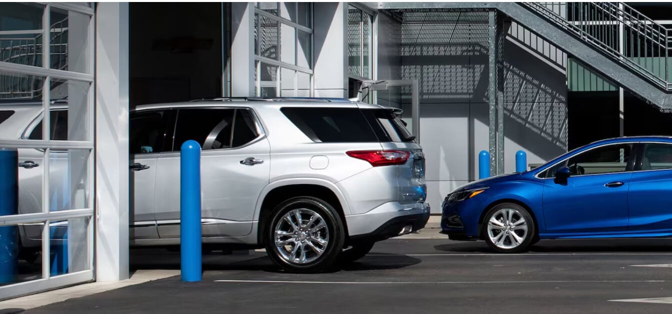 Chevrolet Traverse Silver Ice Metallic and Chevrolet Cruze Kinetic Blue Metallic showing side profiles outside a dealership service bay.