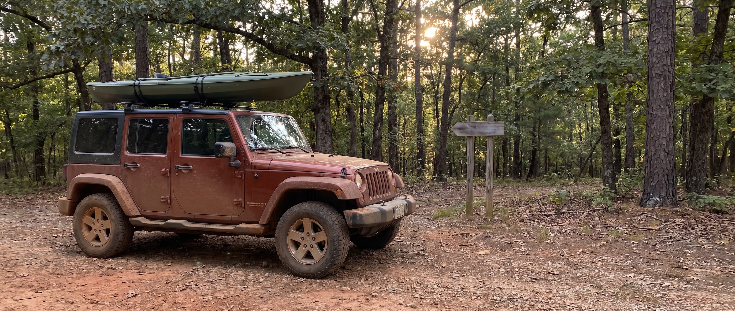 Used Jeep Wrangler Unlimited at an Alabama forested trailhead with kayak on roof rack