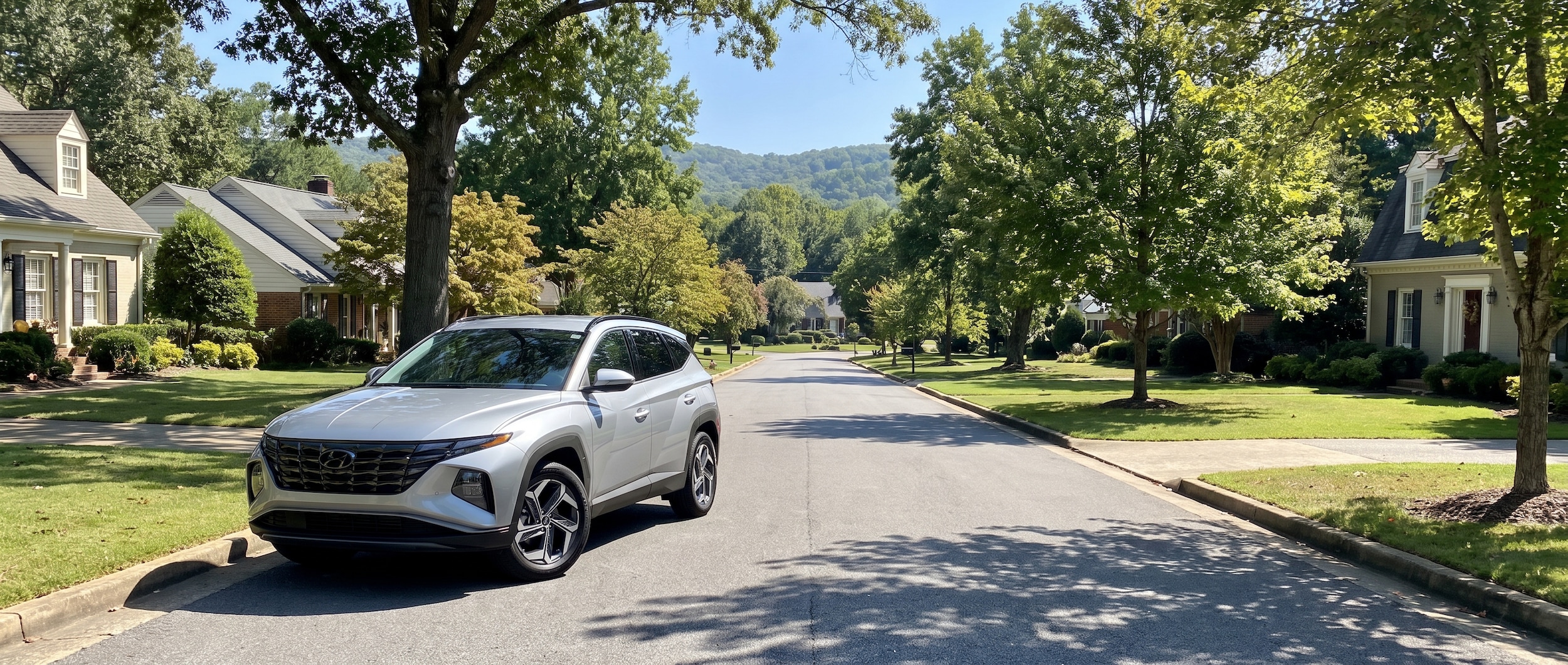 A 2026 Hyundai Tucson in silver parked on a tree-lined suburban street in Vestavia Hills, Alabama, with the characteristic rolling hills and mature tree canopy visible in the background on a sunny summer day