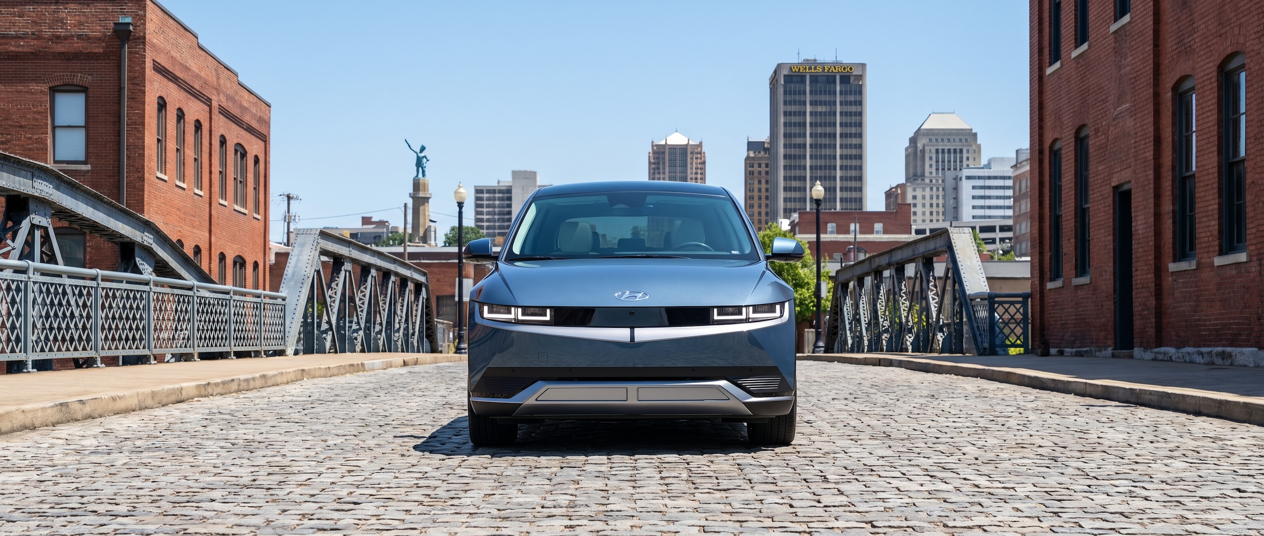 A 2026 Hyundai IONIQ 5 in Cosmic Blue Pearl parked in an urban Birmingham, Alabama setting on a bright summer day, with the city skyline visible in the background and a public DC fast charger in the foreground