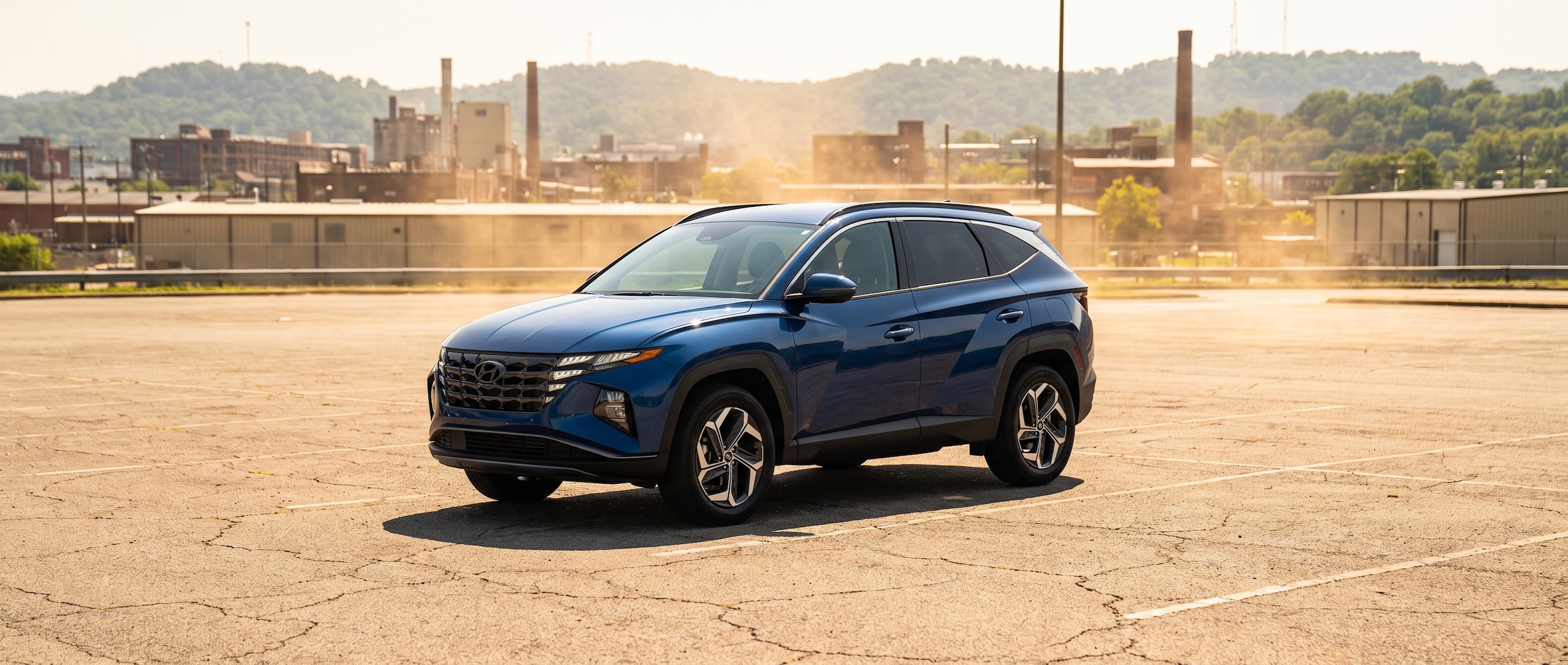 A 2026 Hyundai Tucson in a deep blue metallic finish parked in a sun-drenched Birmingham, Alabama parking lot with summer haze visible in the background, conveying Alabama's intense July heat and the Tucson's compact SUV stance