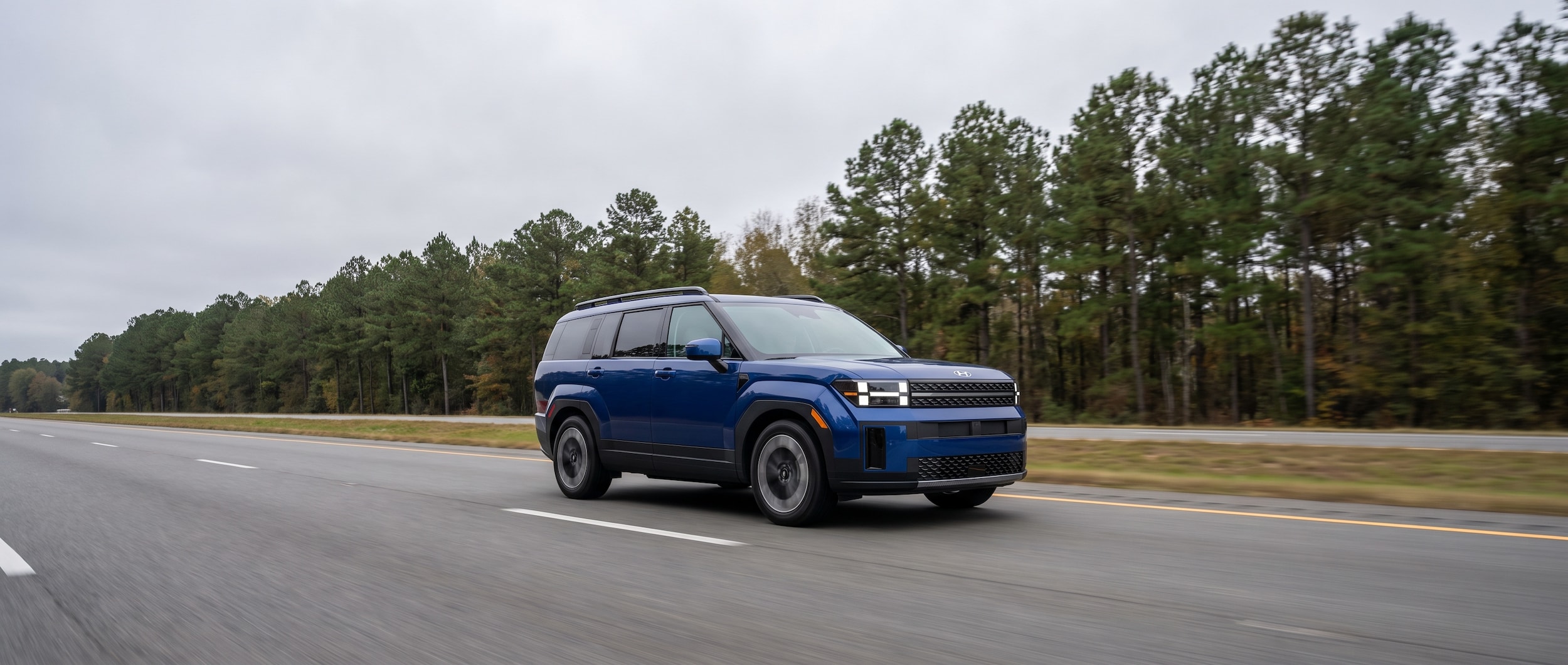 2026 Hyundai Santa Fe Hybrid traveling on a rural Mississippi interstate flanked by pine trees on an overcast morning