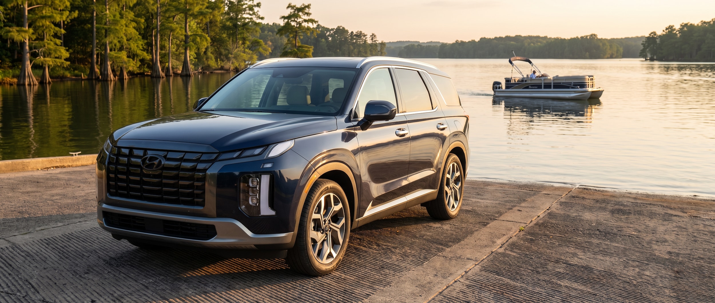 A 2026 Hyundai Palisade in a deep navy or dark gray finish, viewed from a three-quarter front angle, parked on a boat launch ramp at a Tennessee reservoir at golden hour in summer, with a pontoon boat on the water in the background and cypress trees lining the shore