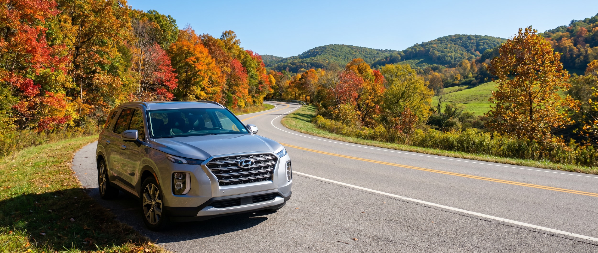 A silver Hyundai SUV parked near a lakeside overlook on a bright summer day, with trees and shimmering water visible in the background, evoking a relaxed Tennessee summer road trip atmosphere.