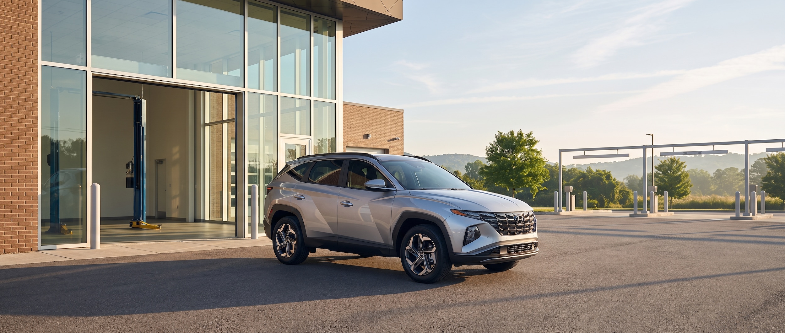 A 2026 Hyundai Tucson parked under a bright Tennessee summer sky outside a clean dealership service bay entrance, with the warm light of a July morning visible and service lane signage in the background